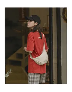 Model wearing a beige crescent canvas crossbody bag with a casual red t-shirt
