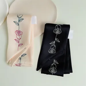 Dettaglio di motivi a rose su sciarpe twilly nere e crema con etichette lavaggio