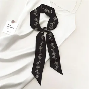Dettaglio di un foulard nero con motivi di rose annodato a fiocco su tessuto di seta