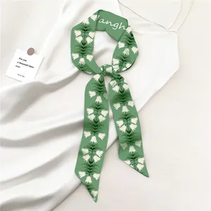Detalle de bufanda estrecha floral verde anudada en vestido de satén blanco con lirio de valles