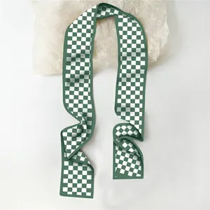 Détail d'un foulard étroit en soie à carreaux verts et blancs avec une texture fluide