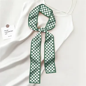 Détail d'un foulard étroit à damier vert noué comme accessoire sur un tissu en soie blanche