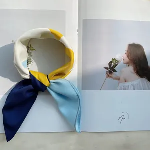 Foulard en soie satinée de 53cm à motif géométrique coloré posé sur un magazine de mode