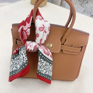 Detail of red and black paisley silk scarf tied on a brown leather handbag handle