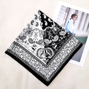Detailed flat lay of a black and white paisley silk scarf on a beige textured surface