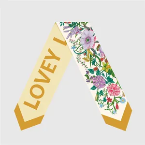 Detalle de pañuelo de seda amarilla con letras LOVEY L y diseños de flores de colores