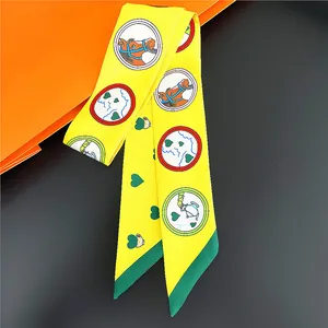 Détail d'un twilly en soie jaune avec motifs de cheval et cœur sur boîte orange
