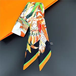 Détail d'un foulard twilly à motif plumes sur boîte orange avec étiquette de soin