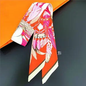 Détail d'un foulard en soie orange avec motif plumes et étiquette de soin sur sac