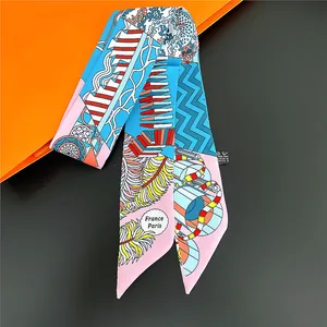 Floral and geometric silk scarf twilly tied in a flat lay with an orange gift box