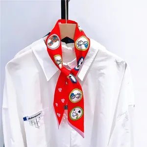 Détail d'un foulard en soie rouge à motifs cœurs noué en nœud sur un col de chemise blanc