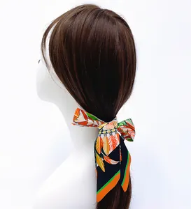Ruban en satin à motif plumes polyvalent, noué comme accessoire de cheveux sur une queue