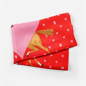 Detail of red silk scarf showing printed horse and pink heart patterns with soft texture