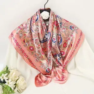 Detail of bohemian paisley print silk scarf in coral pink draped over a white blouse