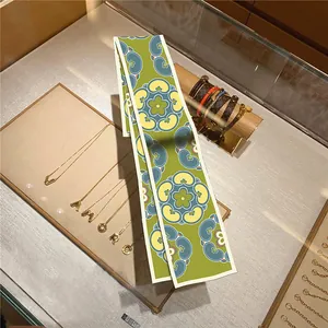 Detail of green floral silk twilly scarf with blue retro patterns on a display stand
