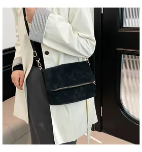 Model wearing a black suede shoulder bag with gold zipper and stylish fold-over design