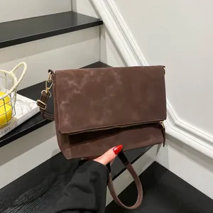 Dark brown suede crossbody bag with flap and adjustable shoulder strap on stairs
