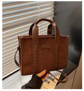 Detail of suede tote bag showing leather TOTE patch and woven strap attachment points