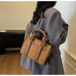 Close-up of brown suede tote bag featuring braided leather straps and embossed logo