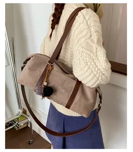 Detailed view of brown suede baguette bag with plush keychain and long leather shoulder strap