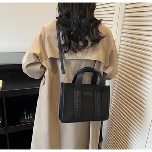 Model wearing a black faux suede tote bag with woven straps and adjustable crossbody strap