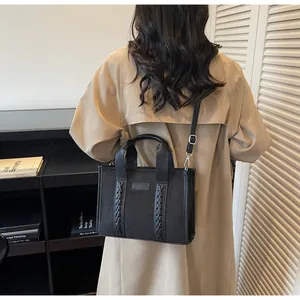 Detail of black faux suede tote bag with woven straps and adjustable crossbody strap on model