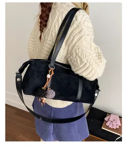 Detail of black suede cylinder bag with fuzzy pom-pom charm worn on a shoulder