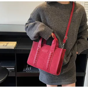Detail of red suede tote bag featuring braided straps, leather TOTE label and silver hardware
