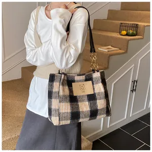 Detail of the plaid tote bag showing bear logo label and golden metal chain strap