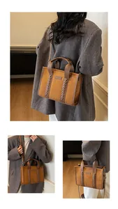 Detail of woven leather accents and embossed TOTE lettering on brown suede tote bag