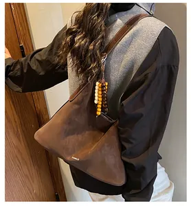 Detail of a brown suede tote bag featuring a beaded charm and a long leather shoulder strap