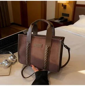 Close-up of brown suede tote bag with woven leather details and embossed metal plaque