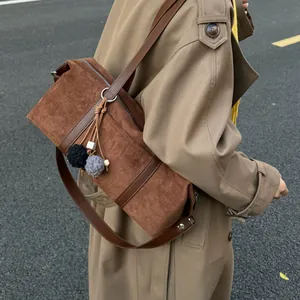 Brown suede baguette bag with plush pompom charms worn by a model in a beige trench coat