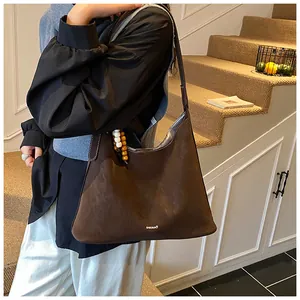 Detail of dark brown suede tote bag featuring a beaded pendant and branded BABUMA logo