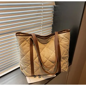 Detail of beige quilted tote bag with brown leather handles in soft window lighting