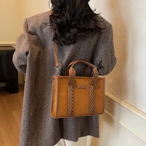 Brown suede tote bag with woven handles and TOTE logo on a grey coat model