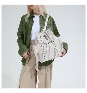 Detail of vintage canvas backpack featuring silver metal rivets and a cross emblem