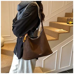 Deep brown faux suede tote bag with wooden bead charm detail worn by a model in interior