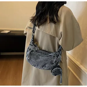 Detail of washed denim crescent crossbody bag with mini round pouch and fringe zipper