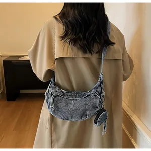 Close-up of washed denim crescent crossbody bag with mini pouch on khaki trench coat
