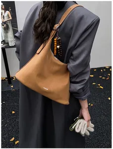 Close-up of brown suede tote bag featuring wooden bead pendant and brand logo
