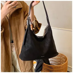 Close-up of black suede tote bag with contrast stitching and decorative bead charm