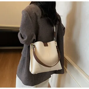 Détail du sac seau en cuir crème avec poignée marron et rivets de protection sur le fond