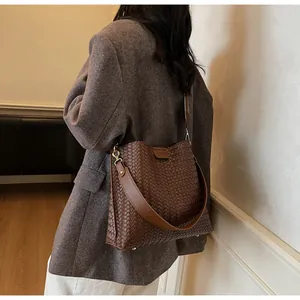 Détail d'un sac seau marron tressé avec large bandoulière et anneaux en métal argenté