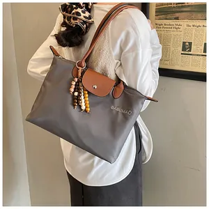 Détail du sac cabas en nylon avec rabat en cuir et perles décoratives porté à l'épaule