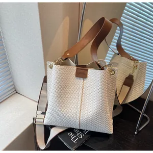 Vue détaillée du sac seau tissé blanc avec poignées en cuir et bandoulière texturée
