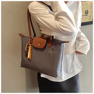Détail du cabas en nylon gris avec poignées en cuir marron et pendentif en perles de bois
