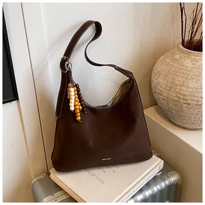 Detail of dark brown matte leather hobo bag with contrast wooden bead charm and logo