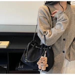 Detail of black quilted bucket bag with chain strap and teddy bear charm on side