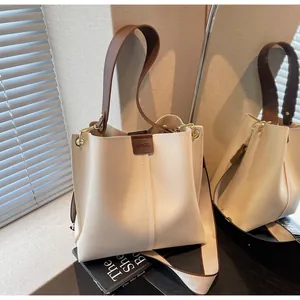 Détail du sac seau crème montrant la poignée marron contrastée et le logo avec ombres